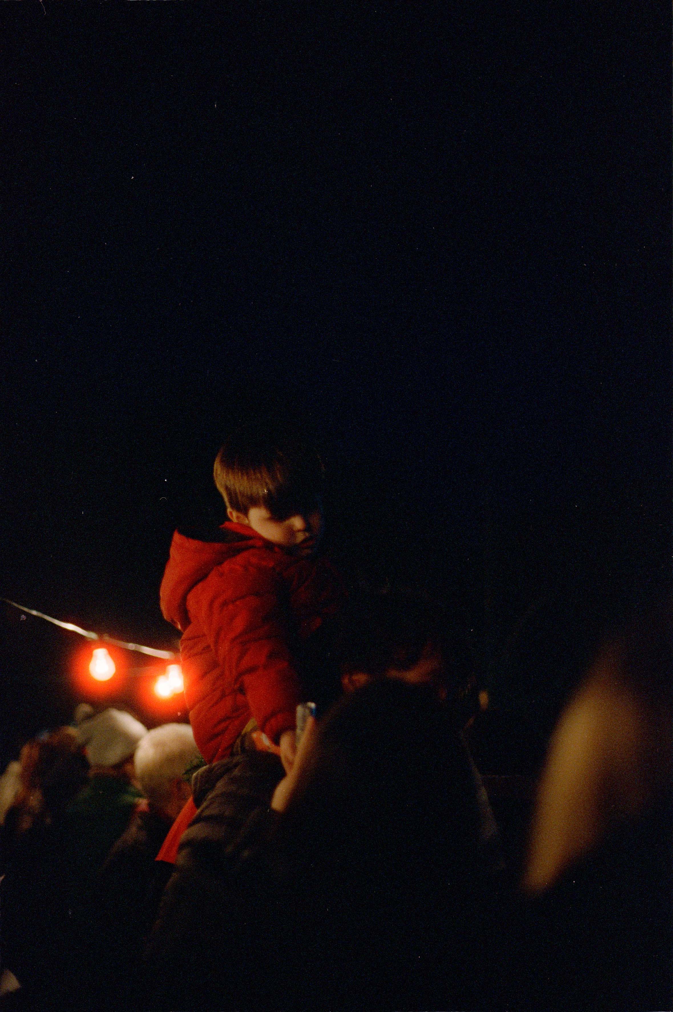 Young boy scarcely illuminated, sat on shoulders