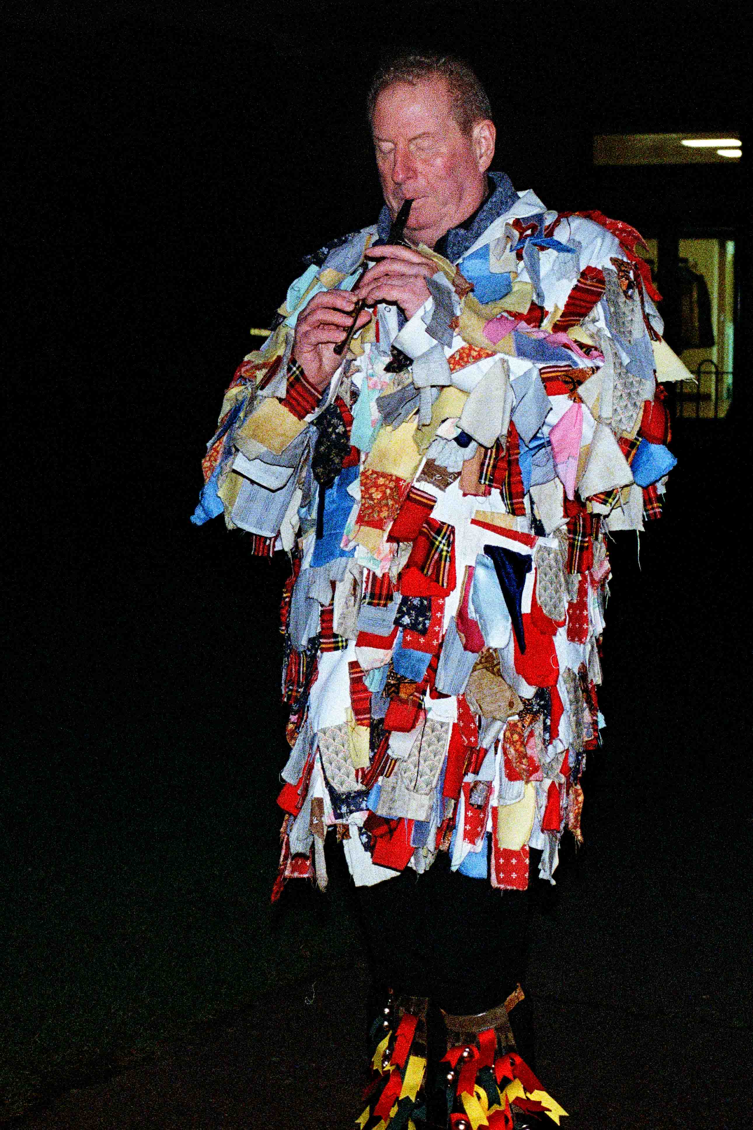 Rag coat morris man plays the flute outside in the dark
