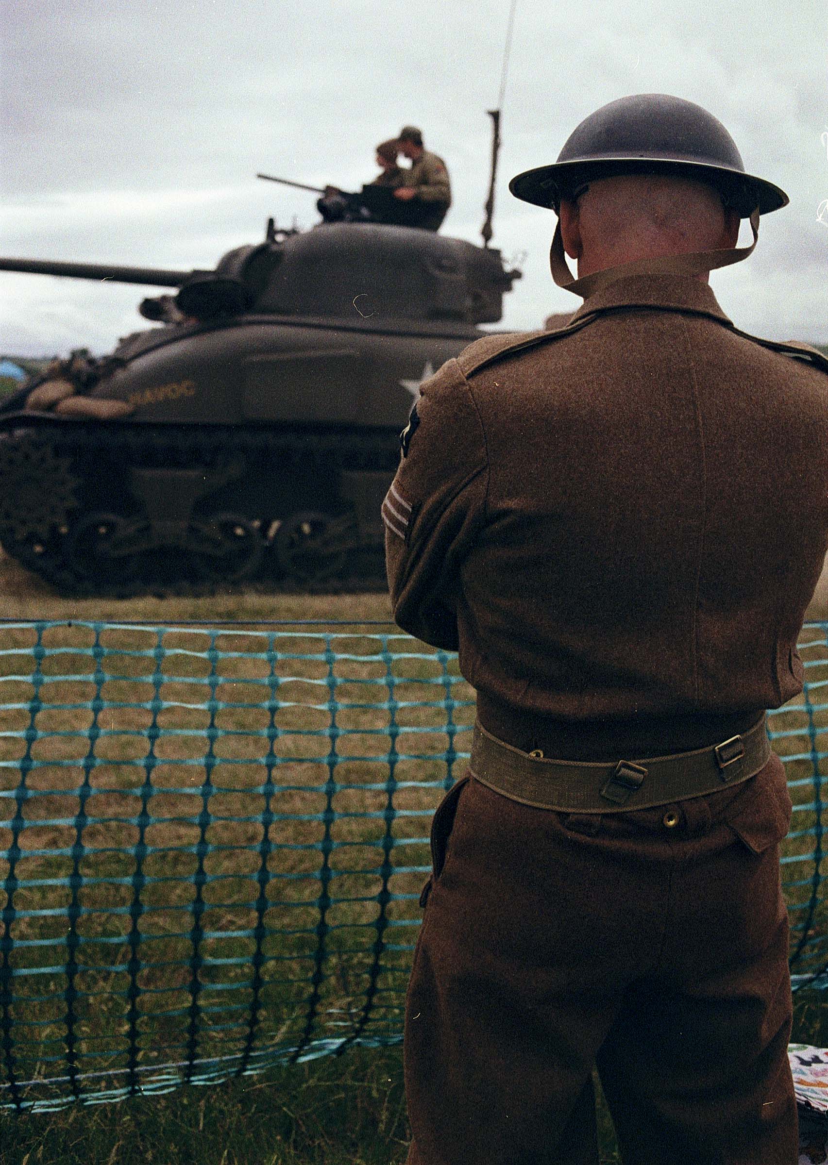 A British soldier seen from behind watches a tank pass