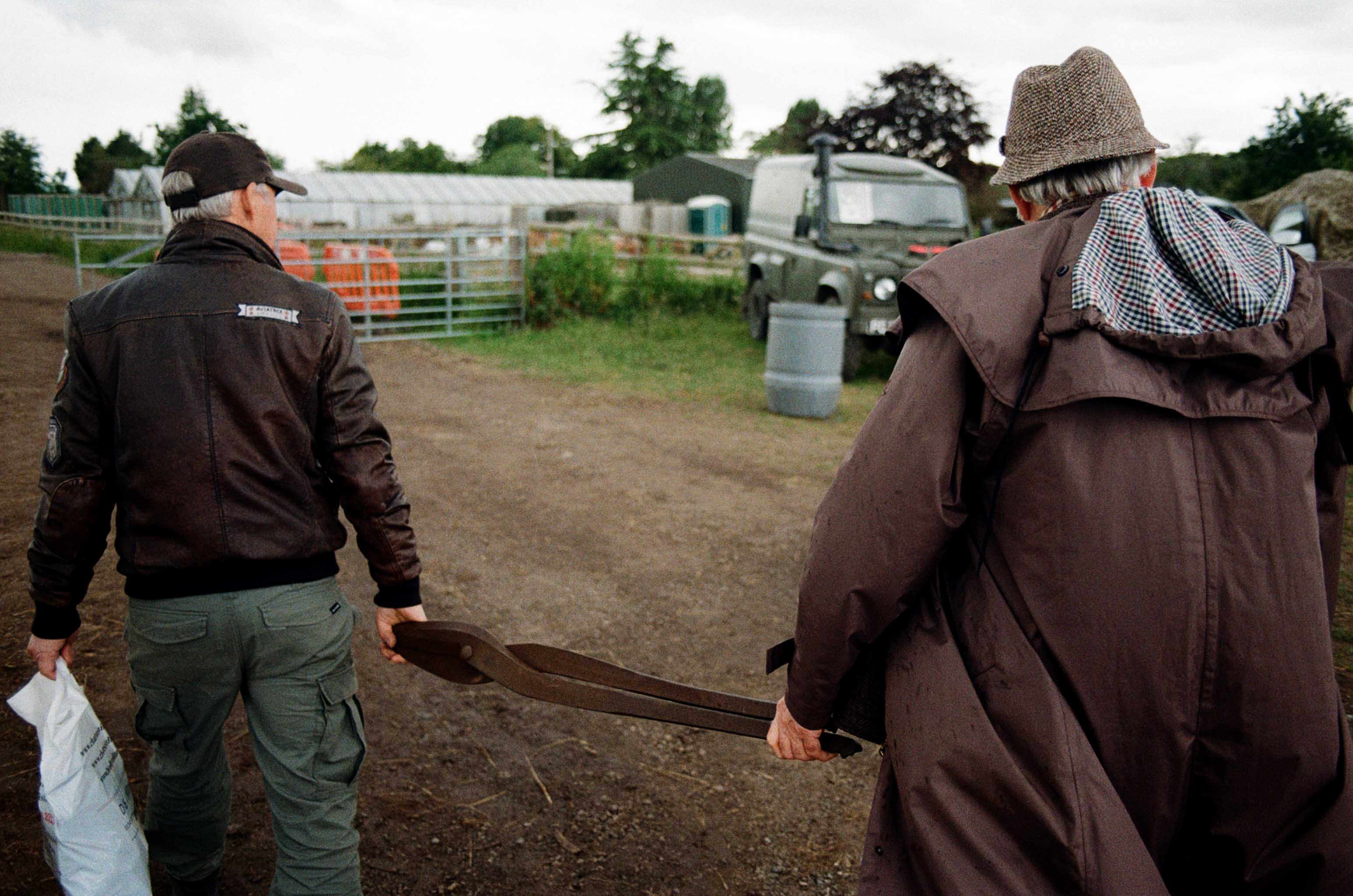 two men in coats carry a rusty metal tool